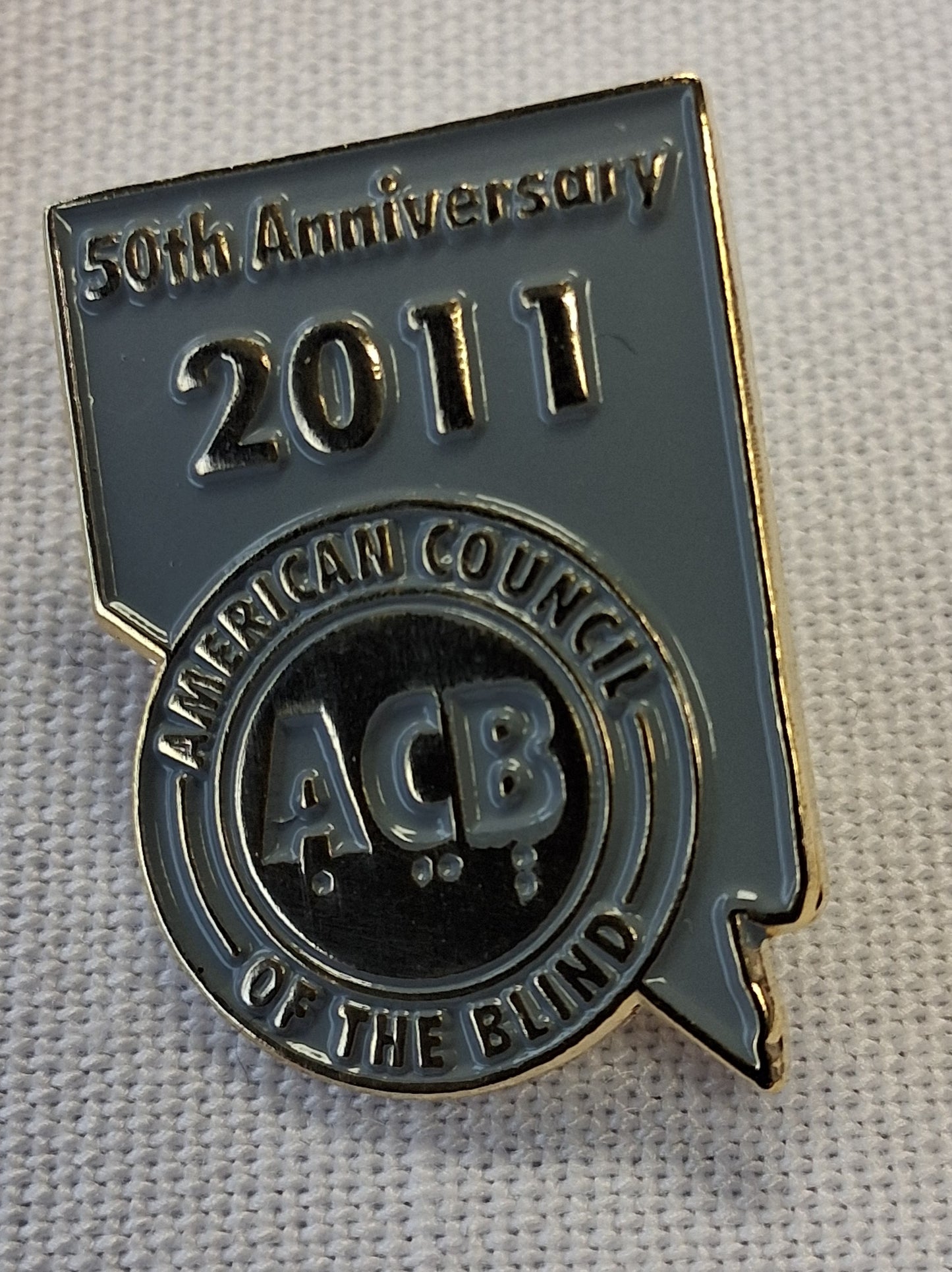 Pin with '50th Anniversary 2011 American Council of the Blind' text on a textured background