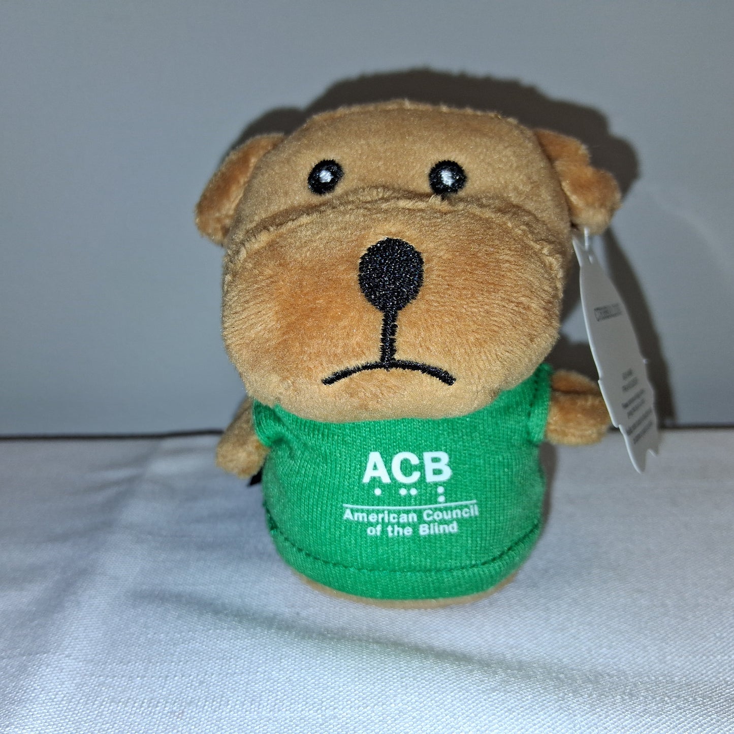 Plush dog toy with a green shirt and 'ACB' logo on a white background