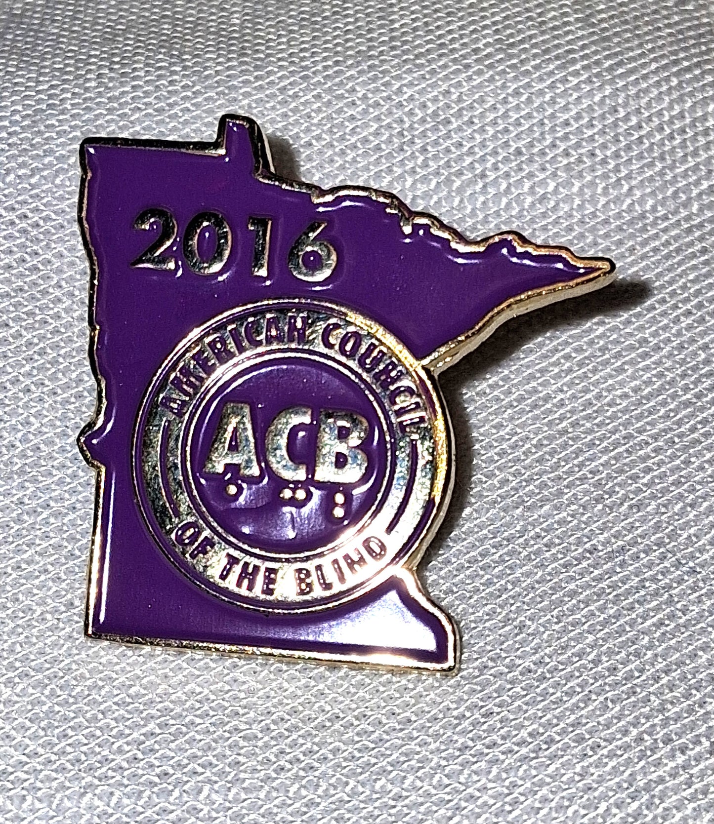 Purple and silver badge shaped like the state of Minnesota with '2016 American Council of the Blind ACB' text on a textured white background.