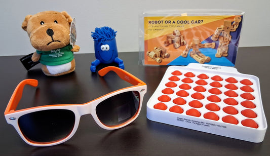 Collection of items including sunglasses, toys, and a board game on a dark surface.